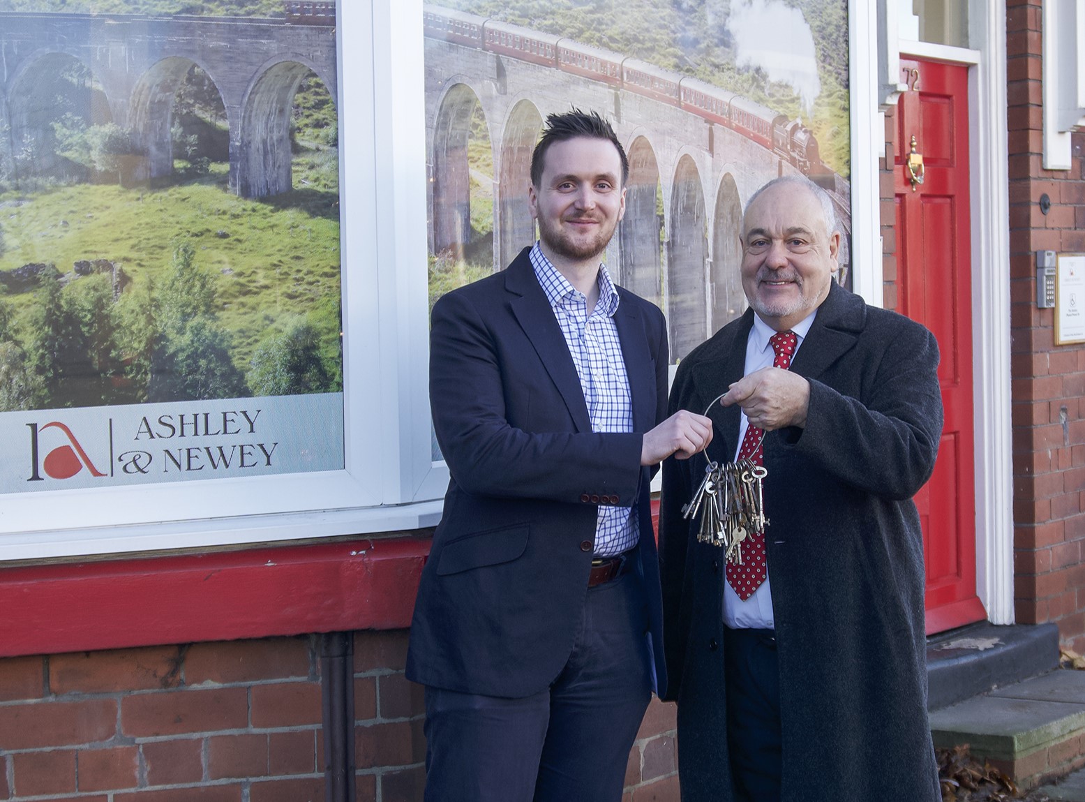 The new owner and exiting founder pose with a set of keys